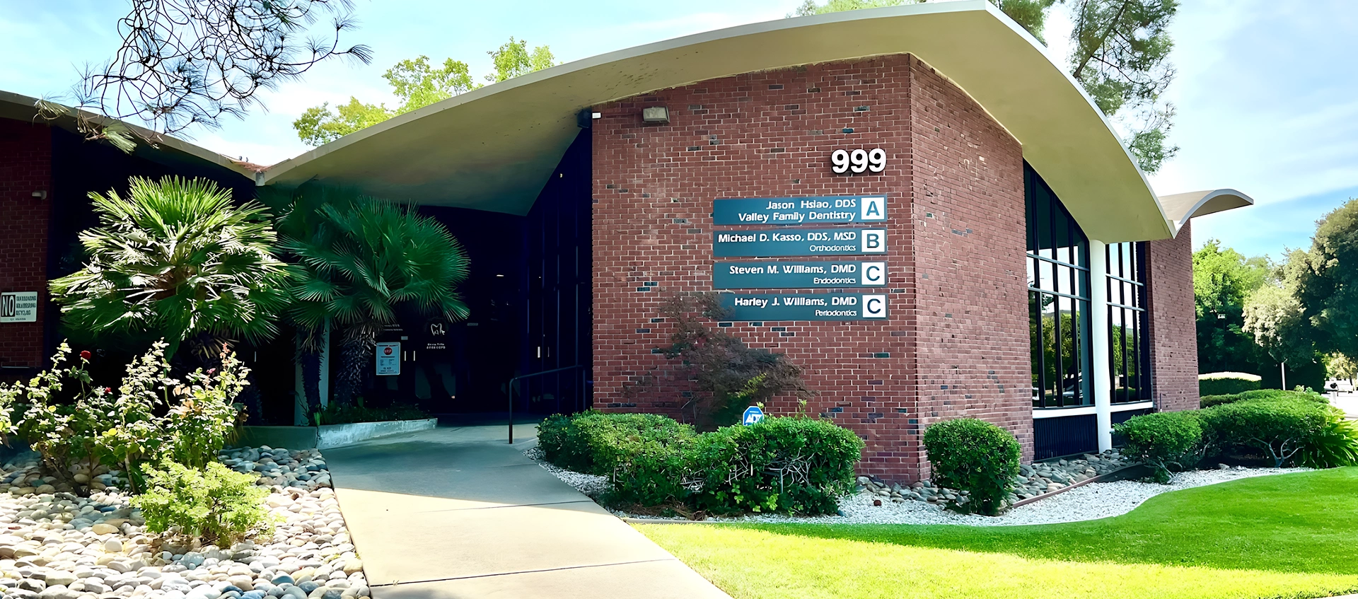 Exterior view of a brick dental office building with landscaped grounds, curved roof, and entrance walkway.