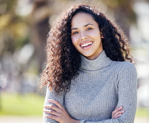 Smiling woman with curly hair wearing a gray sweater outdoors.