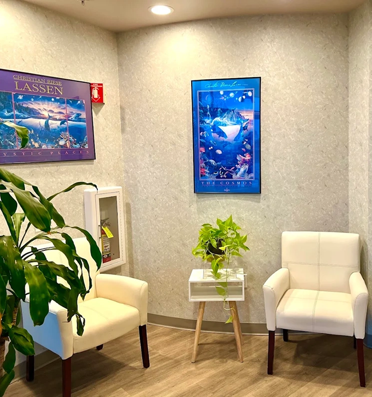 Comfortable waiting area with two white chairs, plants, and illuminated aquarium displays.